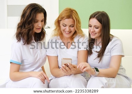 Medical workers or fellow cosmetologists in white uniform look at the phone and laugh. Horizontal photo