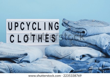 Lightbox with text Upcycling clothes on a blue background. Heap of used denim to donate and recycle. Decluttering. Circular and ecological fashion concept. Zero waste. High quality photo