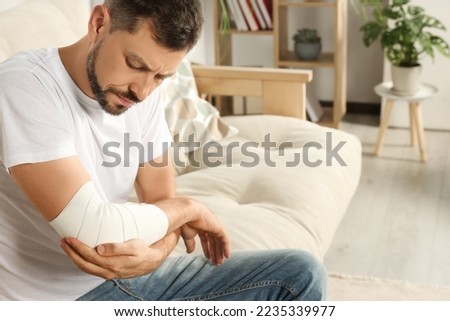 Man with arm wrapped in medical bandage at home Royalty-Free Stock Photo #2235339977