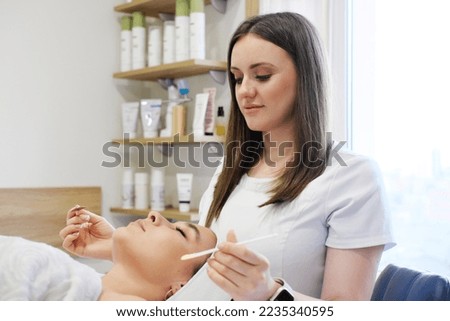 beautician applies cosmetic product to patient woman with brush. Horizontal photo