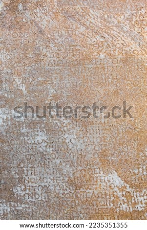 Fragment of ancient greek inscription, carved on marble block at the archaeological site of Ephesus. Selcuk, Turkey (Turkiye). Selected focus. Ancient art and history concept. Retro background Royalty-Free Stock Photo #2235351355