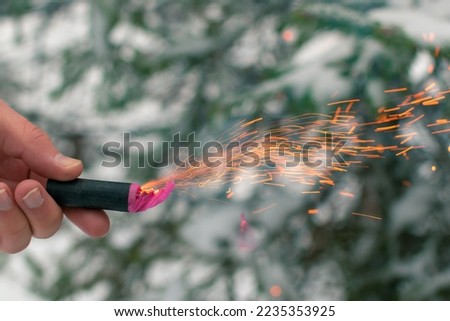 Burning Firecracker in a Hand. Guy Holding a Petard Outdoors in Winter at Daytime. Loud and Dangerous New Year's Entertainment. Hooliganism with Pyrotechnics. Noise of Firecrackers in Public Places Royalty-Free Stock Photo #2235353925
