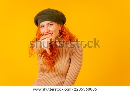 Red-haired woman in a beret in studio on a yellow background, copy space, throwing an ok