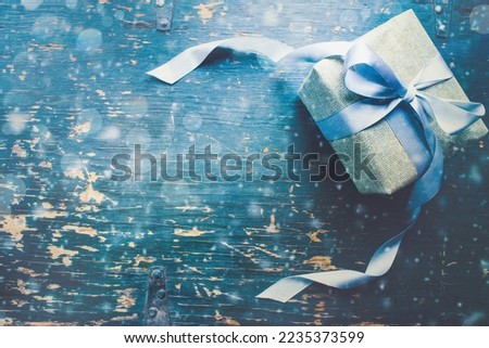 Christmas present with long flowing blue satin ribbon over rustic background. Overhead table top view. Copy space available.