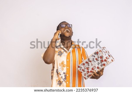 Happy African American male wearing glasses isolated on white studio background holding a wrapped birthday present, laughing black man in spectacles
