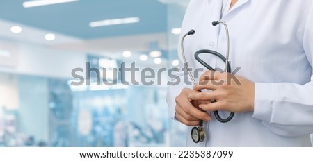 The doctor is standing and holding a stethoscope on a blurred background.