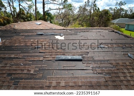Wind damaged house roof with missing asphalt shingles after hurricane Ian in Florida. Repair of home rooftop concept Royalty-Free Stock Photo #2235391167