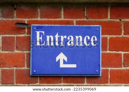 Blue entrance sign with directional arrow. Entrance signage on brick wall of building 