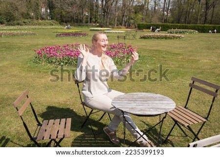 young woman in a beige jumper takes a selfie in the park with blooming tulips