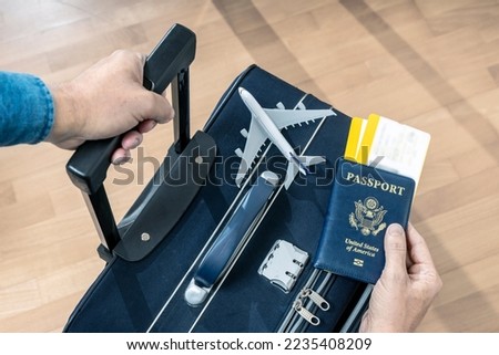 PASSENGER HOLDING USA PASSPORT, TWO BOARDING PASSES AND A SUITCASE AT THE AIRPORT READY TO FLY. TRAVEL INSURANCE FOR BUSINESS AND VACATIONS. Royalty-Free Stock Photo #2235408209