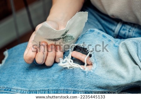 A woman mends jeans, sews a patch on a hole, hands close-up.Mending clothes concept,reusing old jeans. Royalty-Free Stock Photo #2235445133
