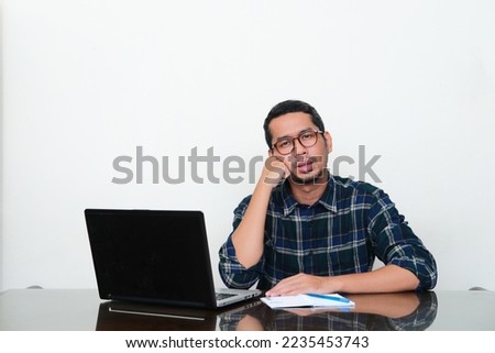 Adult Asian man sitting in his working desk with lazy gesture