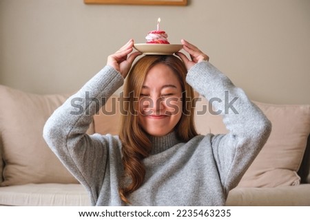 Portrait image of a young woman holding and putting birthday cake with candle on her head