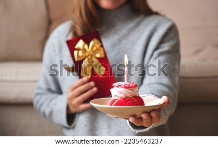 Closeup image of a young woman holding and giving a gift box and birthday cake with candle