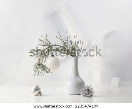 Monochrome Christmas still life: pine branch in a white vase, Christmas decorations, abstract.