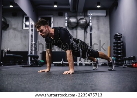 Modern training concept on electrical muscle stimulation. Side view of a male wearing an EMS suit and doing arm exercises and push-ups. He is in a plank position and he touching the floor with hands Royalty-Free Stock Photo #2235475713