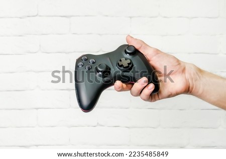 man holds black wireless game controller in his hand, gamepad for remote control of video games. Hand demonstrates a gamepad, top view, light background, space for text
