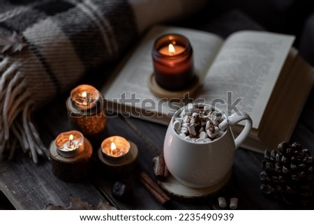 Autumn cozy home composition with hot chocolate with marshmallow and candles. Aromatherapy on a grey fall morning, atmosphere of cosiness and relax. Wooden background, books, close up.