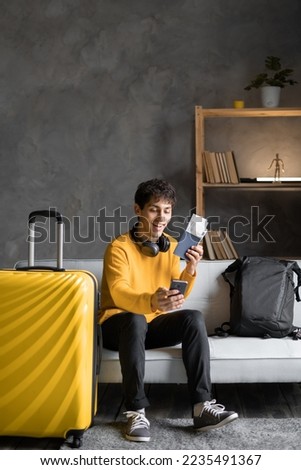 Young man blogger with yellow suitcase taking selfie, getting ready for vacation at home. Happy male traveler making mobile photo of herself, traveling abroad, copy space