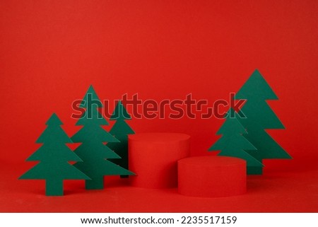 Bright New Year and Christmas stage with red cylinder podium mockup, green paper spruces as forest in modern minimal style for presentation cosmetic produce, gift, goods, design, poster, card, flyer.