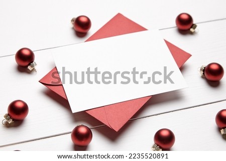 Christmas greeting card mockup with envelope and red balls on white wooden background. Holiday card mockup, closeup