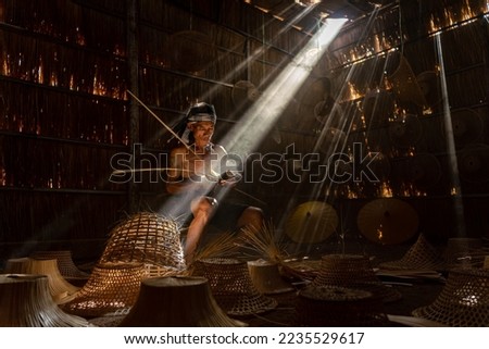Asian village lifestyle concept. A male asian mature adult worker weaving bamboo basket and woven hat under the beautiful sun rays in a room in Sakon Nakhon, Northeast Thailand, Isan way of life. Royalty-Free Stock Photo #2235529617