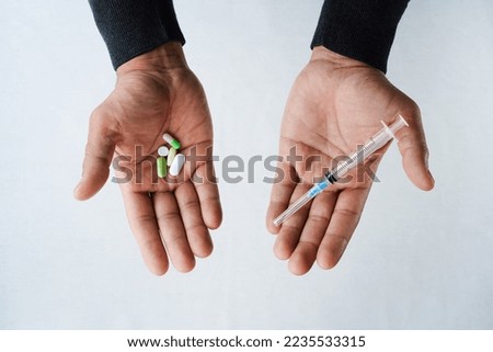 Man's palms pills, syringe. Outstretched hands of brown skin, in one several different tablets capsules, in the other a syringe, top view, close-up, white background. Health concept, choice, balance 