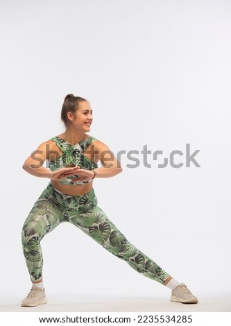 young woman doing fitness exercises on a white background.young bodypositive girl in a green tracksuit demonstrates fitness exercises for body shaping isolated.