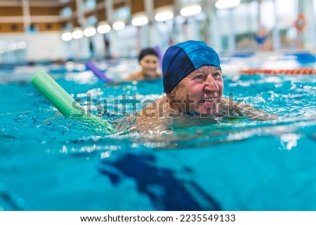 Portrait of smiling happy positive white senior adult man with blue swimming swim cap on his head using foam green pool noodle. Indoor shot. Sports area. High quality photo Royalty-Free Stock Photo #2235549133