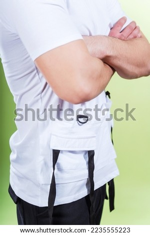 hands of a guy in a white T-shirt on a green background. photo of the details of a summer t-shirt on a plain colored background. photo session of summer clothes in a photo studio