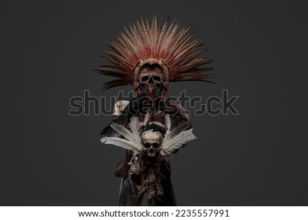 Ancient witch with plumed headdress and staff with skull. High quality photoShot of aztec witch dressed in ceremonial headdress holding staff with skull. Royalty-Free Stock Photo #2235557991