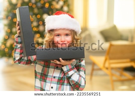 Surprise kid opening Christmas present gift box. Happy funny child in Santa hat holding Christmas gift. Christmas and New Year concept.
