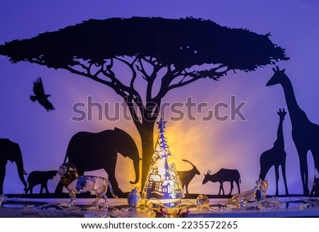 Generic African Safari Silhouette wall art, with  decorative glass illuminated Christmas tree reflecting off the wall to look like an african sunset
