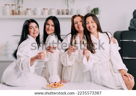 A group of women spend leisure time. Young attractive females in bathrobes drink champagne and chat merrily at home.