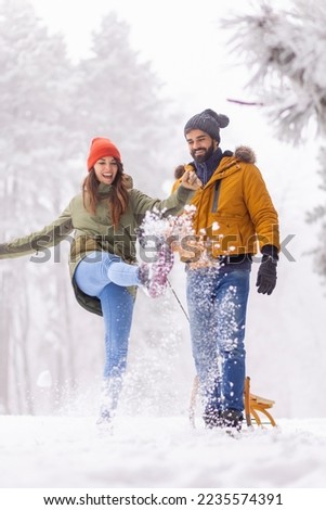 Beautiful young couple in love having fun on winter vacation, enjoying snowy foggy day in the mountain, kicking and throwing snow