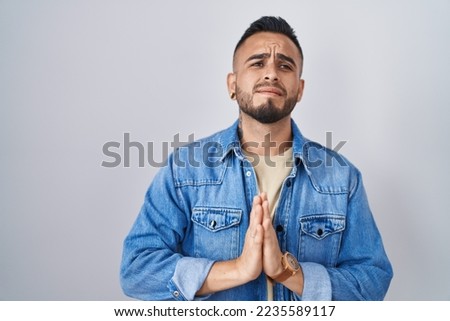 Young hispanic man standing over isolated background begging and praying with hands together with hope expression on face very emotional and worried. begging.  Royalty-Free Stock Photo #2235589117