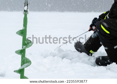Winter fishing on ice. Man jiggling bait in an ice hole. Relaxing in the wild during snowfall.