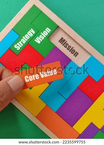 Hand holding orange puzzle with text Core Value and Strategy, Vision, Mission text at wooden puzzle isolated green background. Business finance concept.  Royalty-Free Stock Photo #2235599755