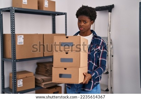 African american woman working at small business ecommerce holding boxes skeptic and nervous, frowning upset because of problem. negative person. 