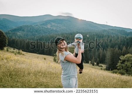 Mom and baby child playing in the mountains. Mother throws up his happy son into sky with his hands. Walking in nature on an autumn day. Family spending time together on vacation. World Tourism Day.