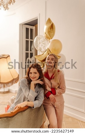 Attractive young caucasian girls in pajamas look at camera spending free time together at home. Girlfriends with long red and blonde hair. Concept of enjoying moment