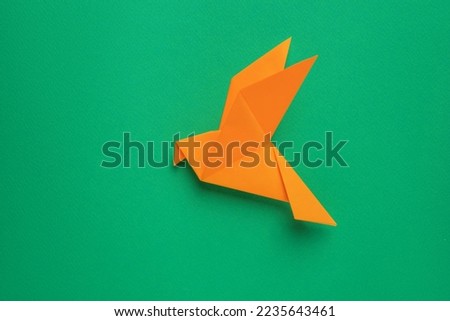 Beautiful orange origami bird on green background, top view