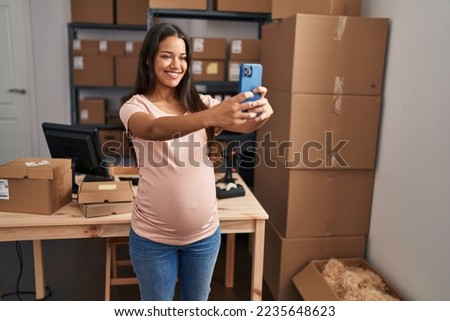Young latin woman pregnant business worker make selfie by the smartphone at office