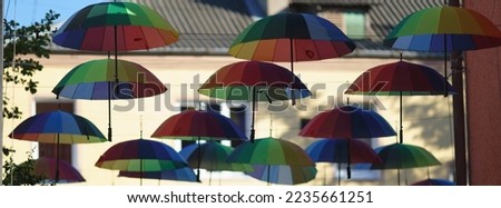 Umbrellas composition. A lot of colorful striped umbrellas hanging on the ropes. Bright green, blue and red colors of them. Theme of the beauty in any weather. Panoramic image