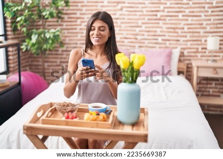 Young beautiful hispanic woman make photo by smartphone to gift breakfast at bedroom