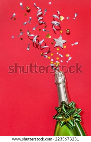Festive bottle of champagne with confetti on red background. Holidays concept