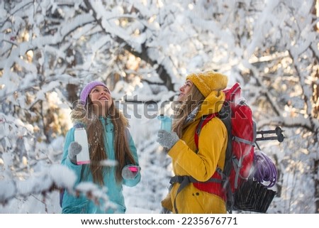 Photo of a mom and daughter during outdoor hiking in winter forest. They make an online video call with smartphone or making selfie.