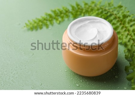 Jar of face cream and plant on wet green surface. Space for text