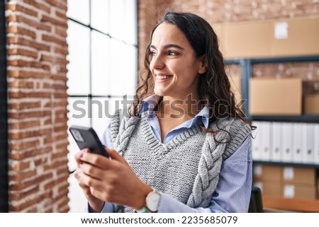 Young hispanic woman ecommerce business worker using smartphone at office