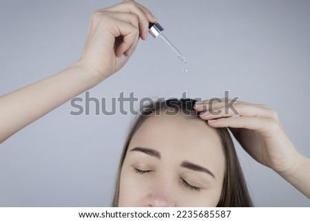 Brunette girl applies oil on her head to strengthen the roots and care for her hair. Means against baldness, brittleness, tarnishing, loss of color, hair strengthening. Concept of care and cosmetology